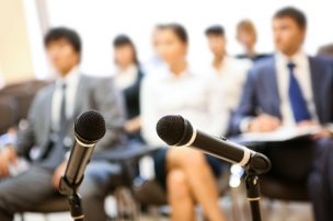 Image of two microphones on background of people listening to lecture at conference