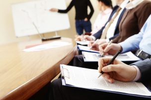 Close-up of businesspeople hands holding pens and papers near table at business seminar